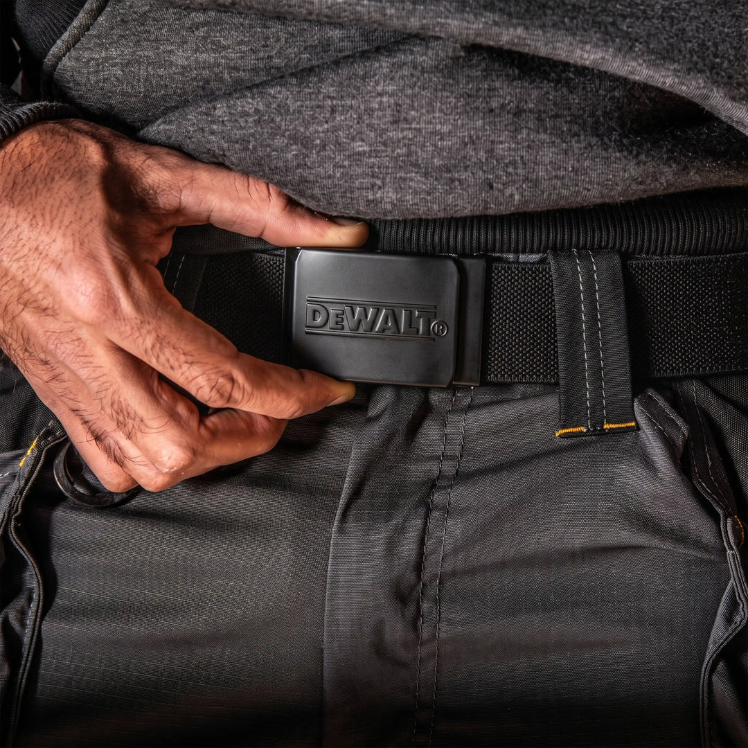 A close-up of a person wearing a black DeWalt belt with a matching black buckle, fastened around dark gray work pants.