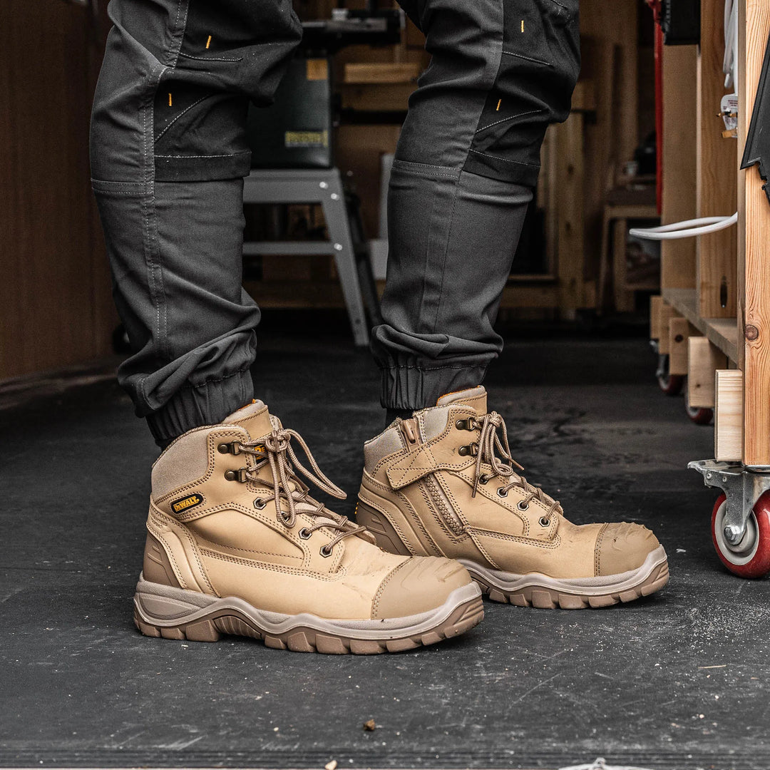 A person wearing tan work boots with dark gray cargo pants in a workshop setting.