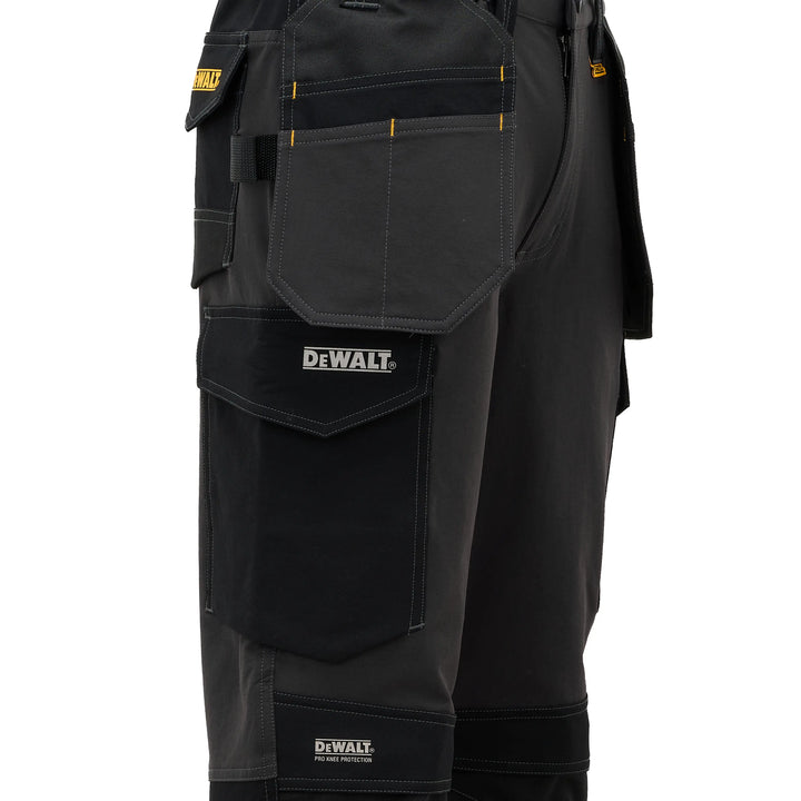 Close-up of black DeWalt work pants showing multiple utility pockets, yellow contrast stitching, and the DeWalt logo on the front pocket.