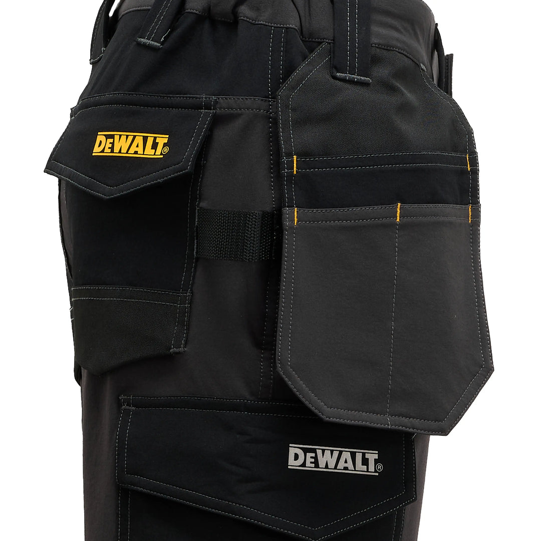 Close-up of black DeWalt work pants showing multiple utility pockets, including a flap pocket with a yellow DeWalt logo and a larger front pocket with a white DeWalt logo.