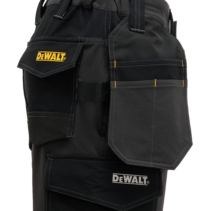 Close-up of black DeWalt work pants showing multiple utility pockets, including a flap pocket with a yellow DeWalt logo and a larger front pocket with a white DeWalt logo.