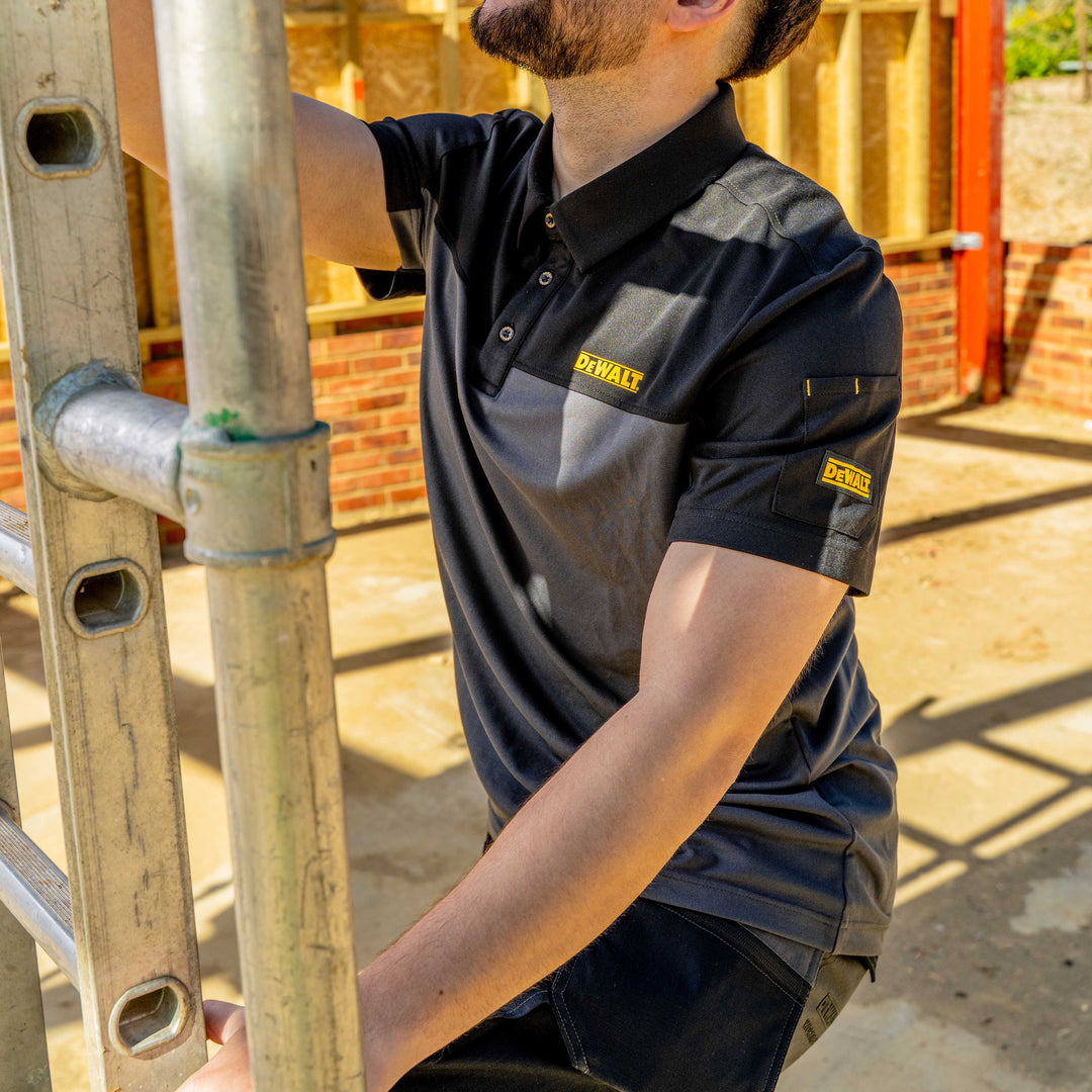 Person wearing a Dewalt shirt holding a metal ladder on a construction site.