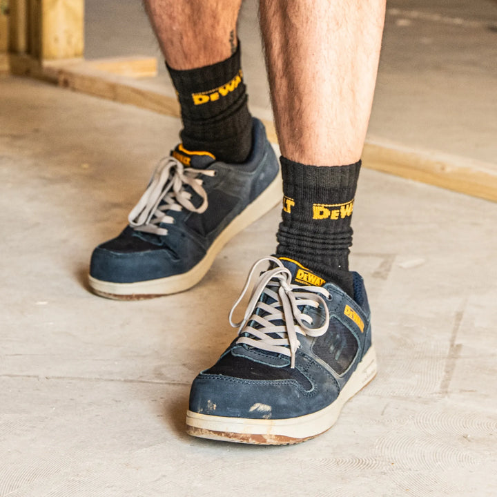 A person wearing blue work shoes and black crew socks with yellow Dewalt branding, standing on a concrete floor.