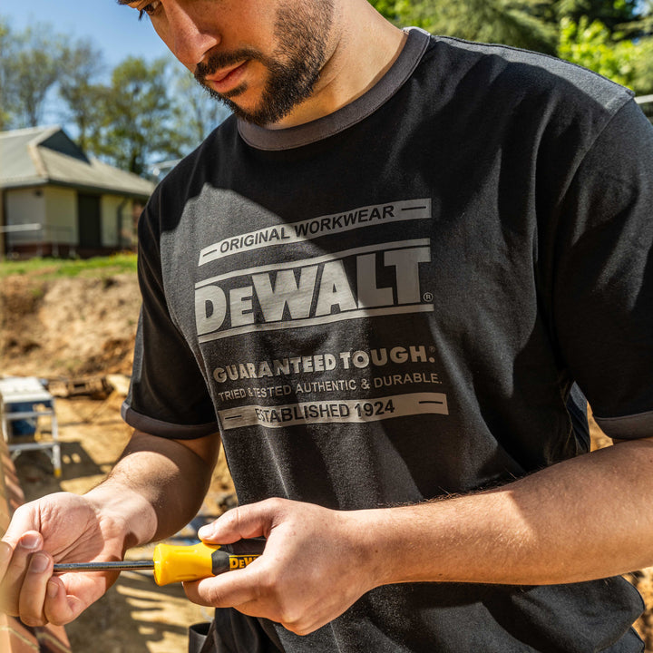 Person wearing a Dewalt t-shirt holding a screwdriver outdoors.