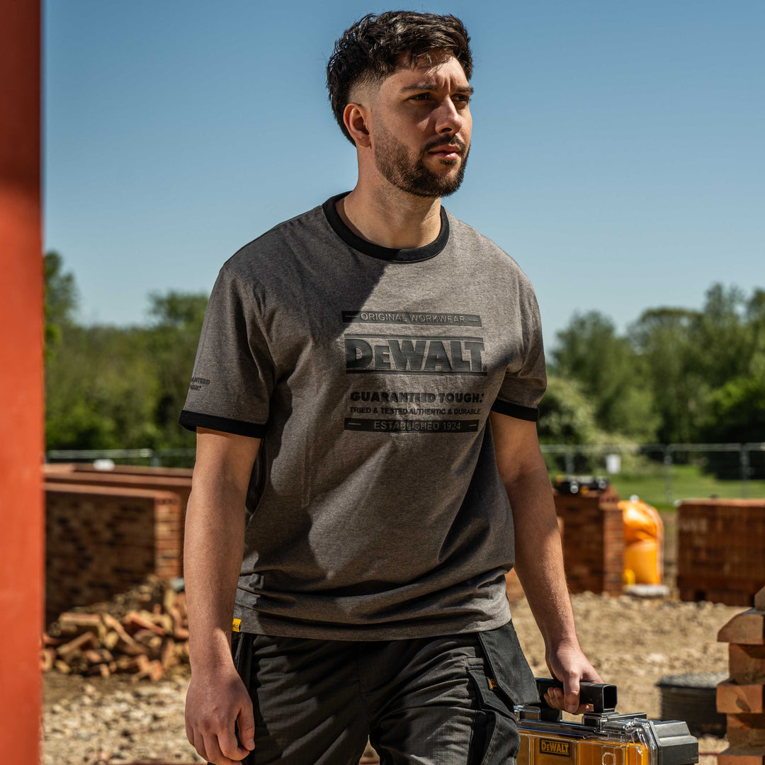 Man wearing a Dewalt t-shirt holding a power tool outdoors.