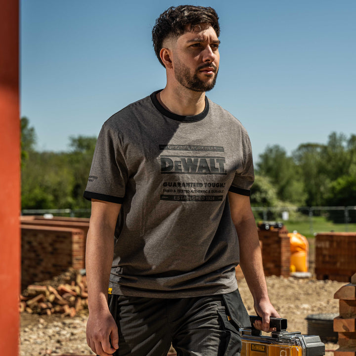 Man wearing a Dewalt t-shirt holding a power tool outdoors.