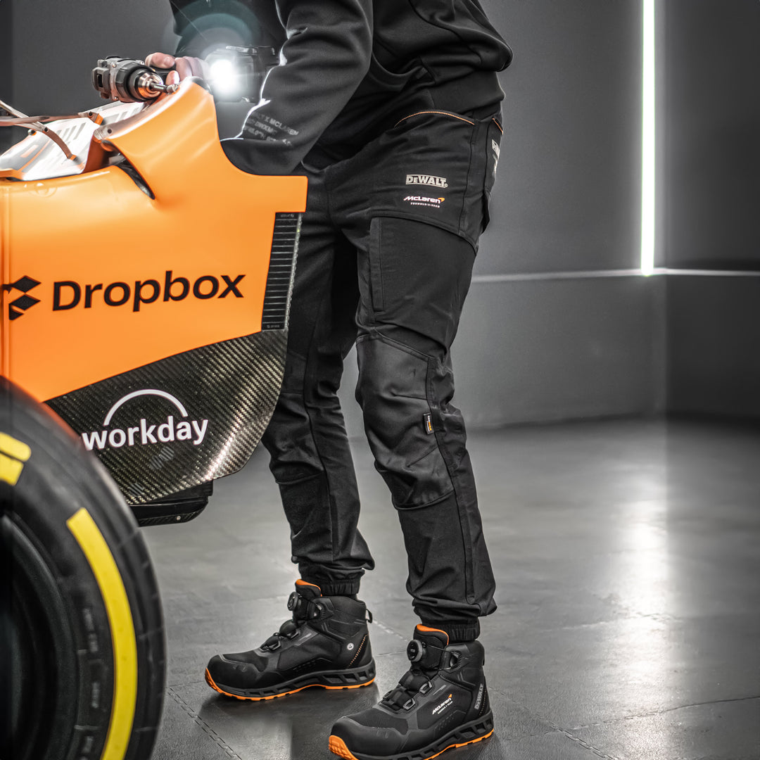 Person in black work pants and boots holding a tool, with Dropbox and Workday logos on a large orange box.