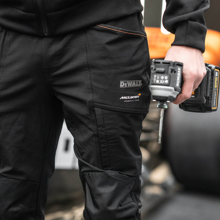 Person wearing black pants with Dewalt logo holding a power drill.